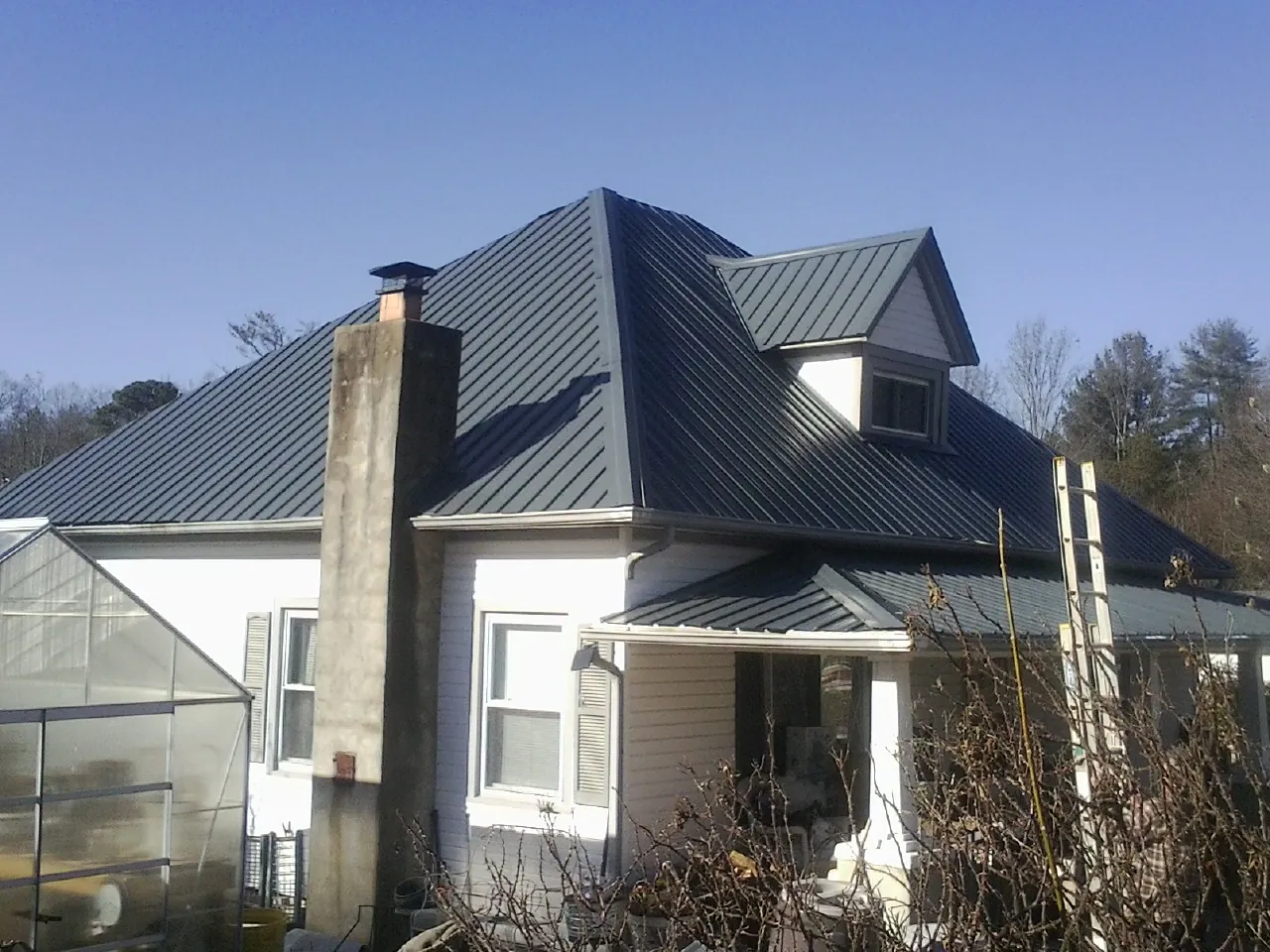 Dark blue standing seam metal roof on a white farmhouse with dormer in Olympia