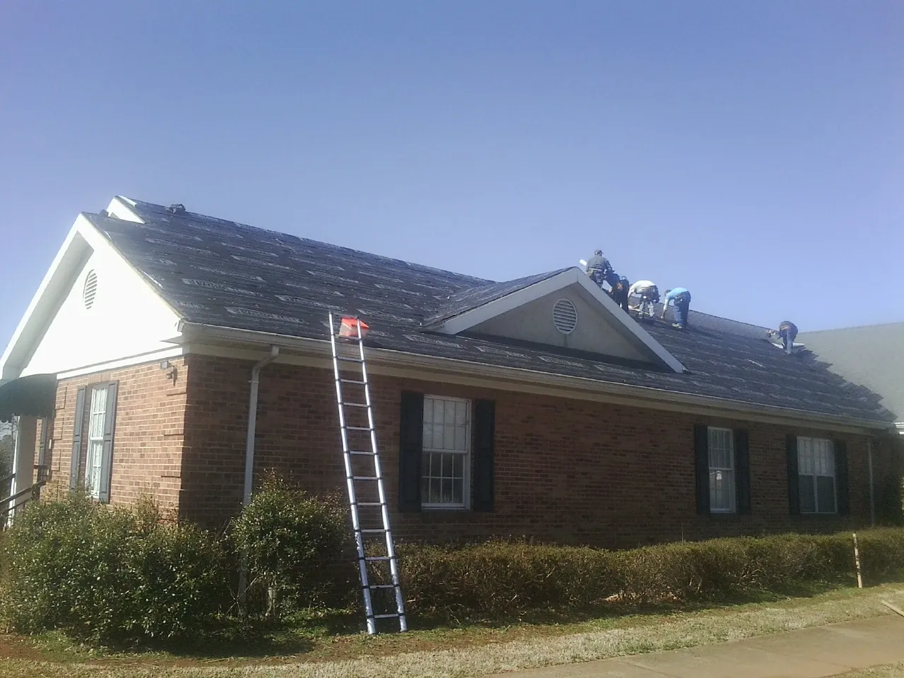 Crew tearing shingles off a brick ranch roof with a ladder set — Metal Roof Repair work by our crew in Olympia