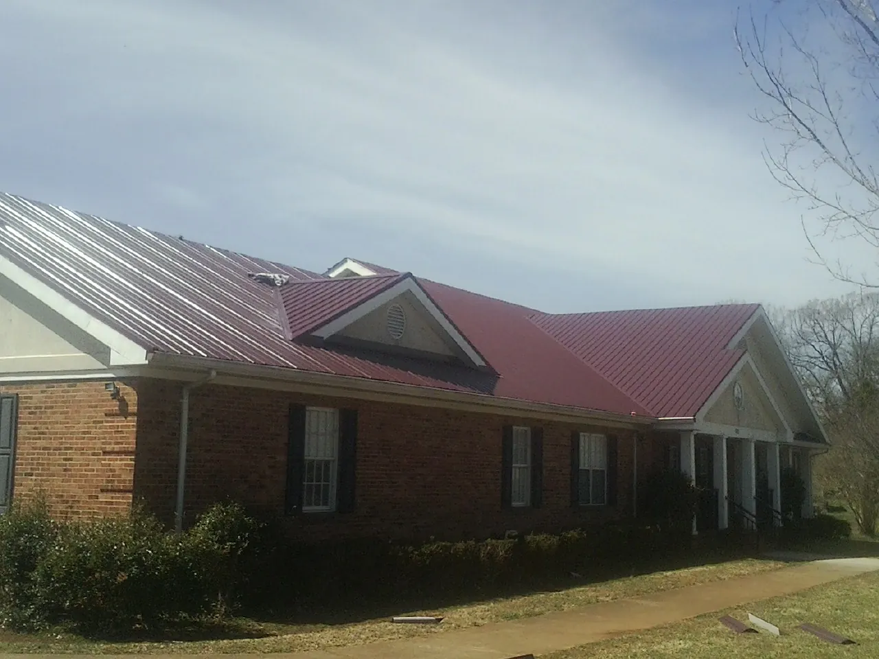 Red metal roof with gabled entries on a long brick building, from a Hail Damage Roof Repair job in Olympia