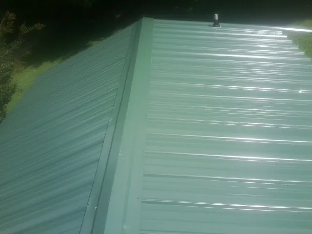 New green metal panels meeting at the ridge of a roof — Flat Roof Repair work by our crew in Olympia