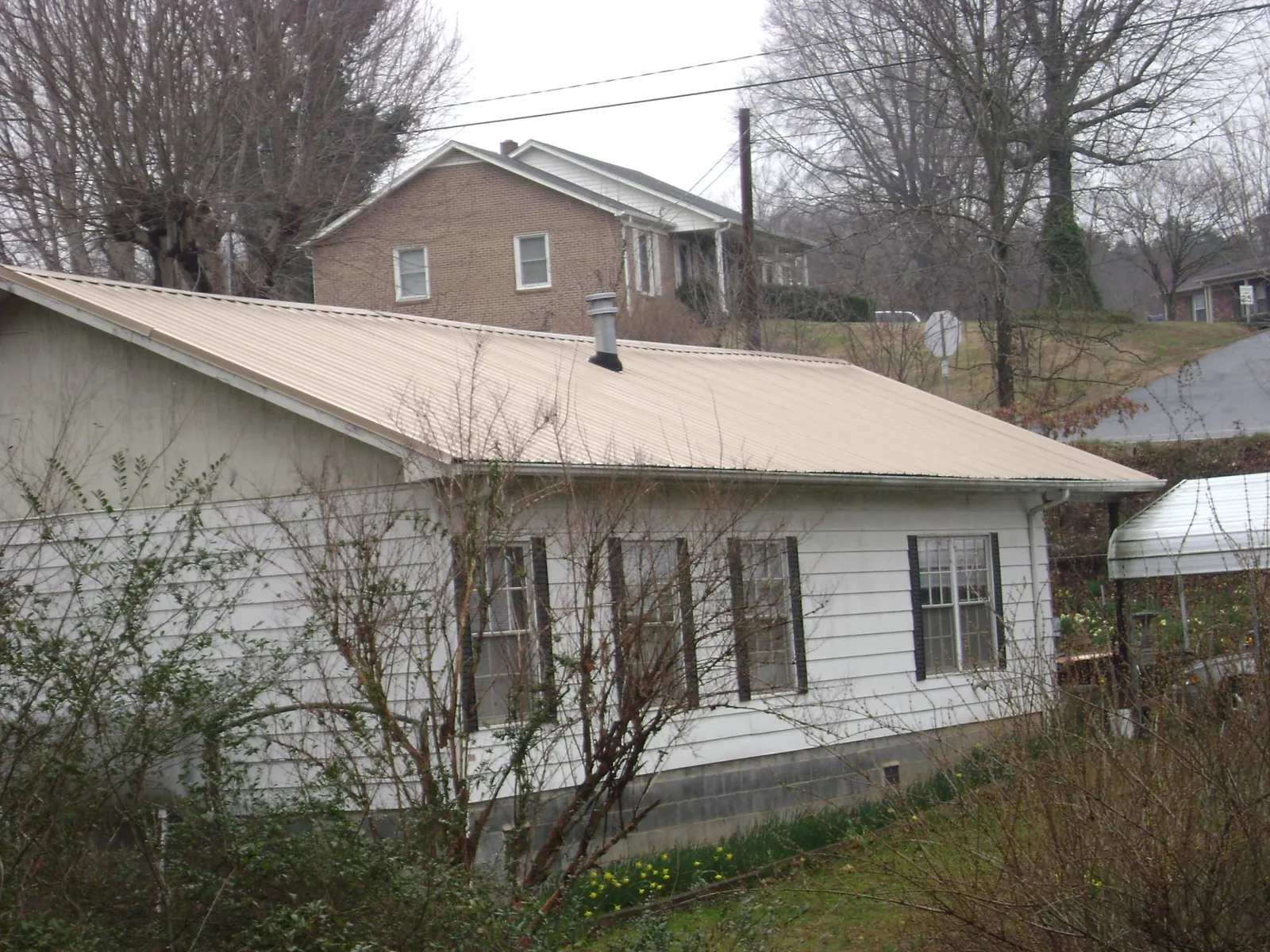 Tan metal roof on a white sided house set into a hillside — Commercial Roofing by Roofing Brothers in Olympia